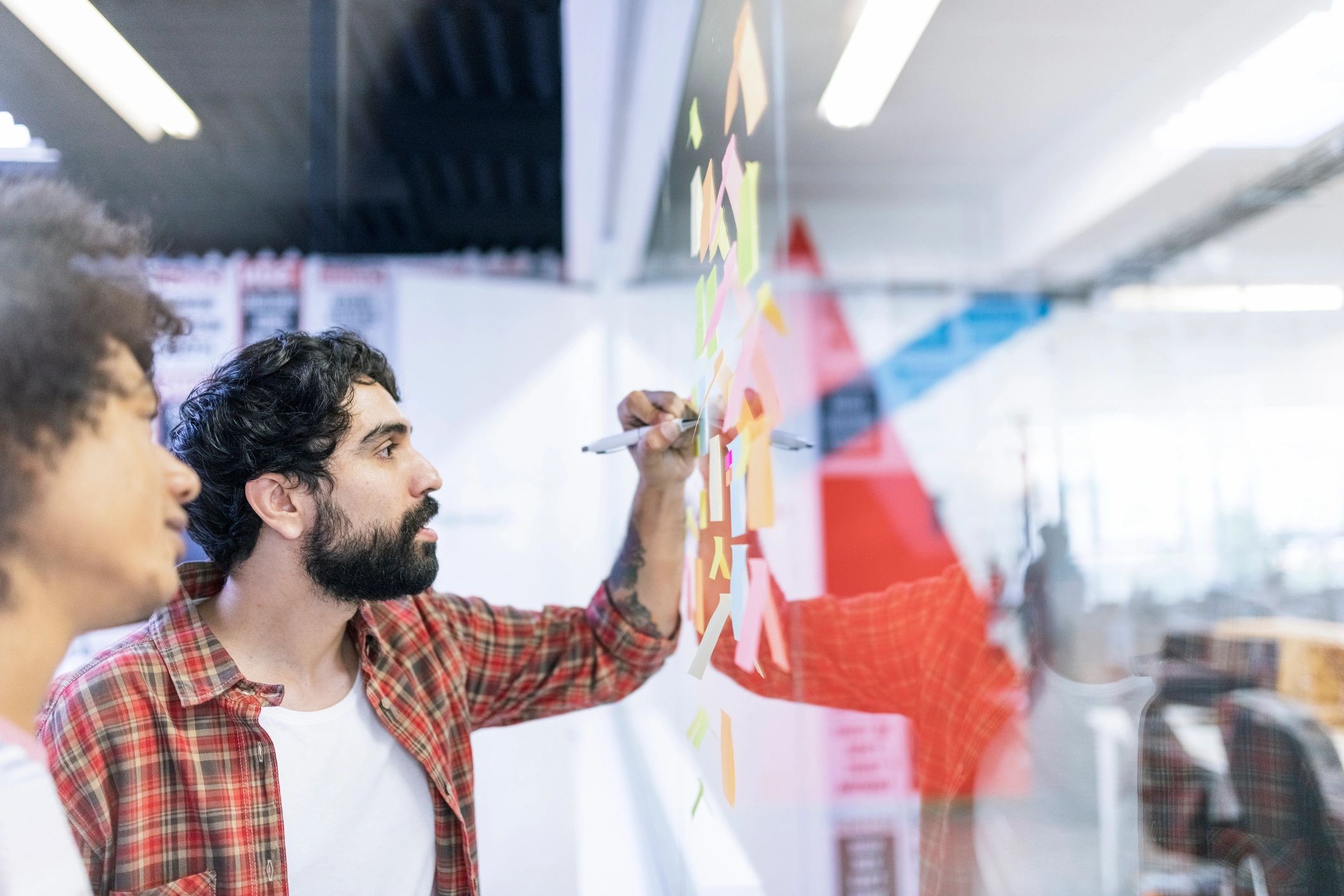 Colleagues planning strategy using sticky notes on a glass wall
